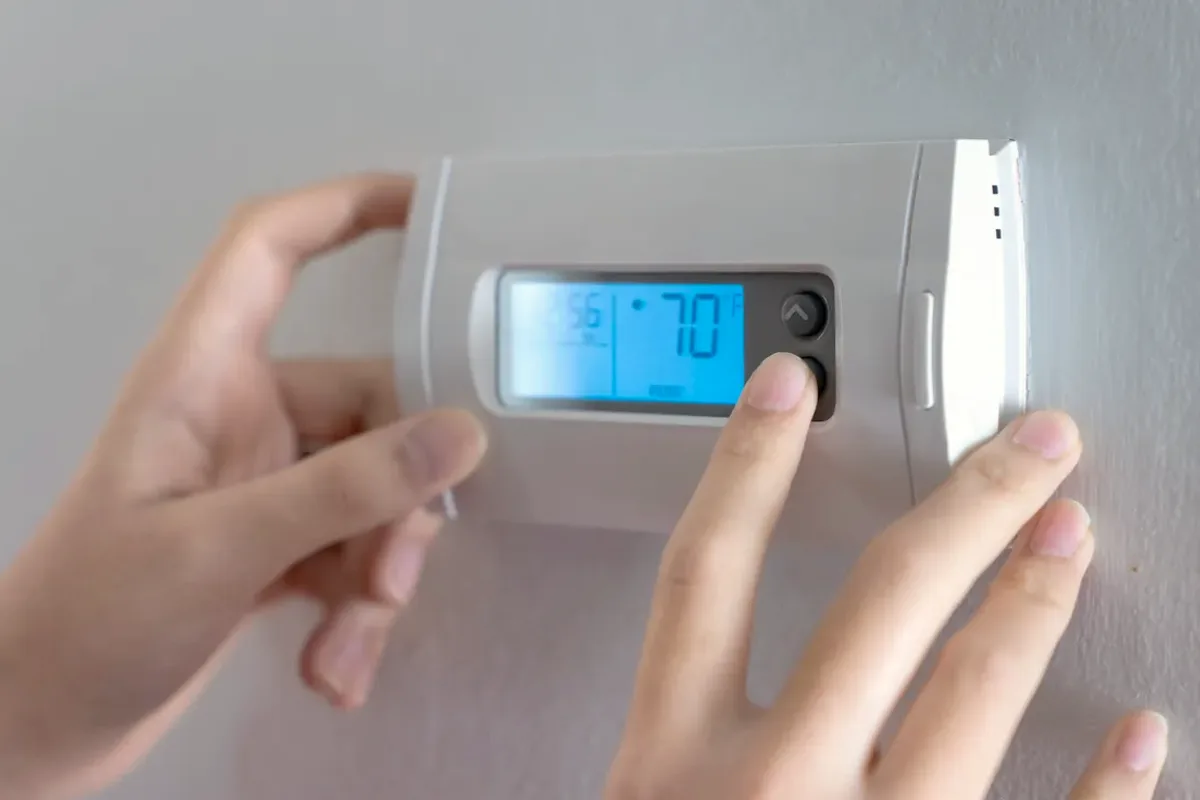 Hands adjusting a digital wall thermostat